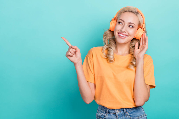 Portrait of optimistic person wear stylish t-shirt hand touch headphones look directing empty space isolated on turquoise color background. - Фото, зображення