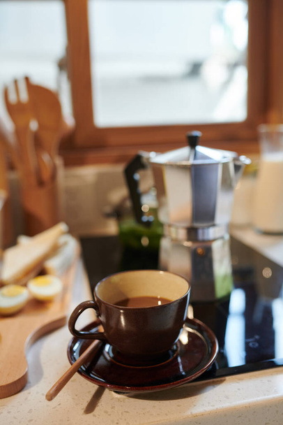 Egy csésze kávé a konyhapulton, a tűzhely mellett, fazékkal a tetején. - Fotó, kép