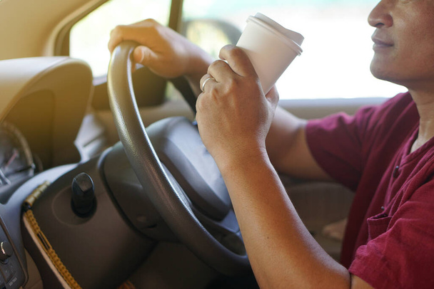 Blízký muž pije kávu z papírového kelímku v autě. Koncept, baverge pro osvěžení nebo pomáhá probudit se ze spánku během řízení, které může způsobit autonehodu. - Fotografie, Obrázek