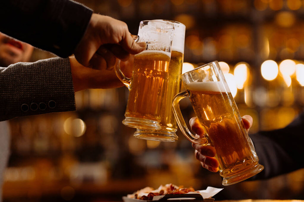 people, drinks concept - close up of male hands clinking beer glasses and pretzels at bar or pub - Foto, Imagem