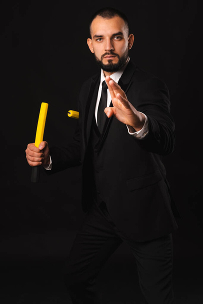 Vertical portrait of a bearded man holding nunchaku performing martial arts over black background. - Photo, Image