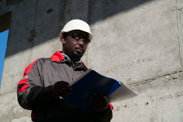 Trabalhador afro-americano fica no canteiro de obras e olha de papéis de trabalho - Foto, Imagem