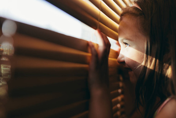 Young girl looking through blinds and smiling - Фото, изображение