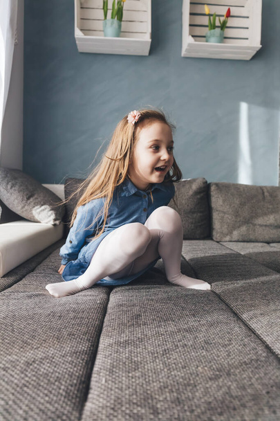 Ευτυχισμένο κοριτσάκι που παίζει στον καναπέ στο σπίτι. Παιδική ηλικία - Φωτογραφία, εικόνα