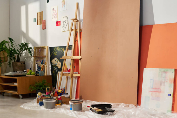 Grupo de suprimentos, equipamentos e outros itens necessários para a pintura recolhidos no chão e ao longo da parede de oficina espaçosa de artista - Foto, Imagem