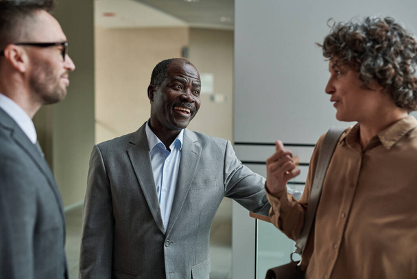 Happy mature African American boss or director of business company lauding one of subordinates during conversation at meeting - Valokuva, kuva