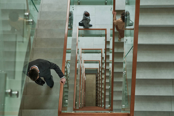Bovenaanzicht van drie zakenmensen in formele kleding die naar boven lopen en tussen trappen in een modern gebouw terwijl ze naar hun werk gaan - Foto, afbeelding