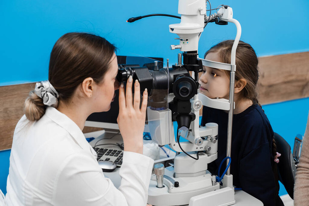 Ophthalmologist illuminates eye of child with light from slit lamp to diagnose the eyes and cornea. Pediatric ophthalmologist with slit lamp examines eyes and cornea of child - Фото, зображення