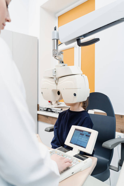 Child looks into phoropter during an eye examination of pediatric ophthalmologist. Phoropter for measuring refractive error and determining information for prescription for eyeglasses - Fotó, kép