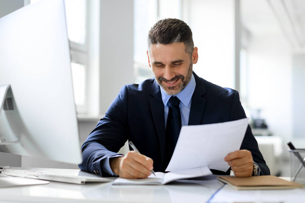 Successful entrepreneurship career. Happy middle aged businessman reading papers and business reports, sitting at workplace in office, accounting and documentation - Photo, Image