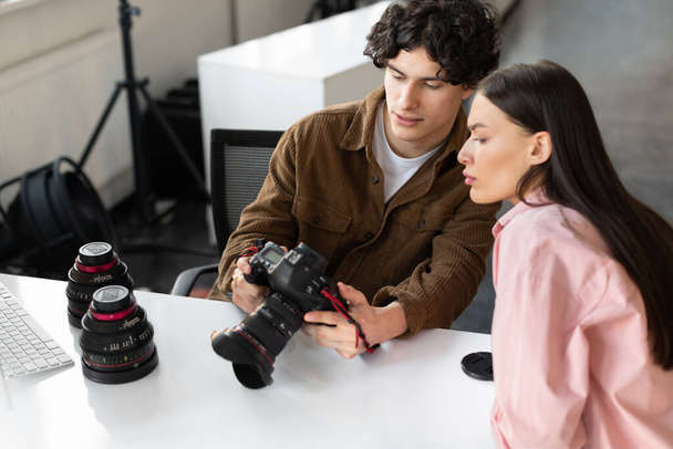 Picture review. Photographer man and yougn female model discussing shots after photoshoot in studio. Cameraman talking to lady to choose the best picture, sitting at workplace - Photo, Image