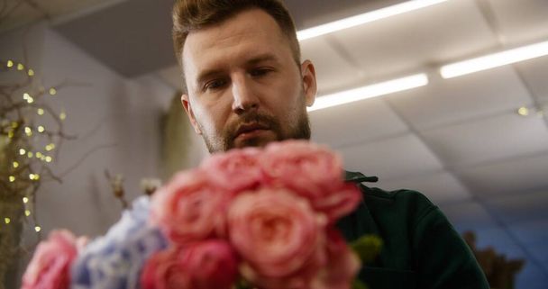 Close up shot of experienced florist working in flower shop. Concentrated man collects beautiful bouquet uses fresh flowers to sale or delivery. Concept of retail floral business and entrepreneurship. - Photo, Image