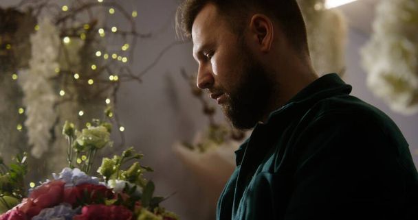 Close up shot of experienced florist working in flower shop. Man creates beautiful bouquet uses branches and flowers. Vases with plants around. Concept of retail floral business and entrepreneurship. - Photo, Image