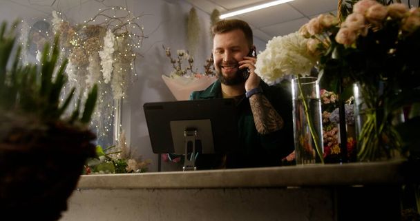 Mężczyzna przedsiębiorca, właściciel, kwiaciarnia rozmawia przez telefon i przyjmuje zamówienia online za pomocą tabletu cyfrowego. Kwiaty w wazonach w kwiaciarni. Kwiaciarnia, kwiatowy mały biznes i koncepcja przedsiębiorczości. - Zdjęcie, obraz
