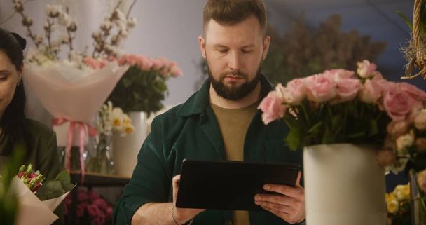 Férfi virágárus számít virágok vázában, és veszi az ügyfél érdekében online digitális tabletta számítógép. Kisvállalkozó, virágüzlet tulajdonosa. A virágüzlet és a vállalkozói szellem fogalma. - Fotó, kép