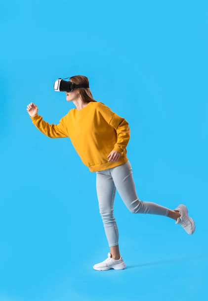 Running young woman in VR glasses on blue background - Photo, Image