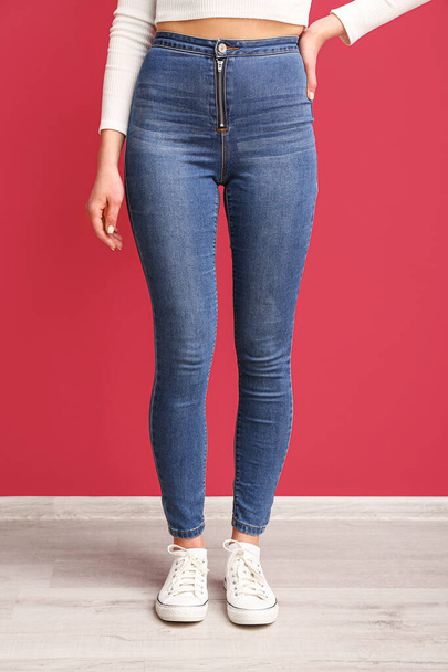 Young woman in stylish jeans near red wall - Foto, Bild
