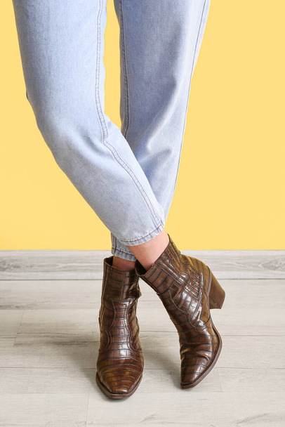 Young woman in stylish jeans near yellow wall, closeup - Photo, Image