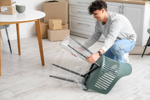 Young man wrapping chair with stretch film in kitchen - Photo, Image