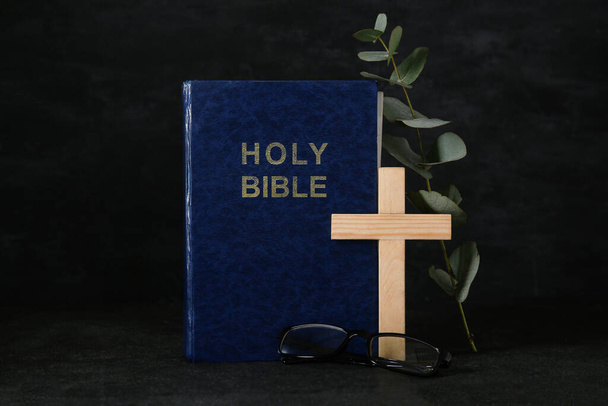 Holy Bible with eyeglasses and wooden cross on black background - Φωτογραφία, εικόνα