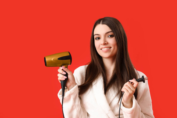 Beautiful young woman with hair dryer on red background - Photo, Image