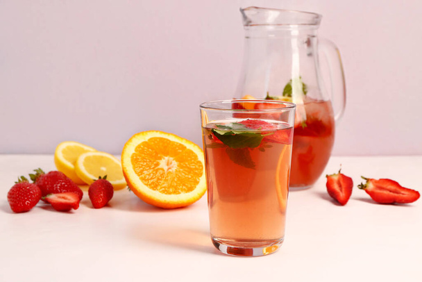 Glass and jug of tasty strawberry juice on white table - Fotó, kép