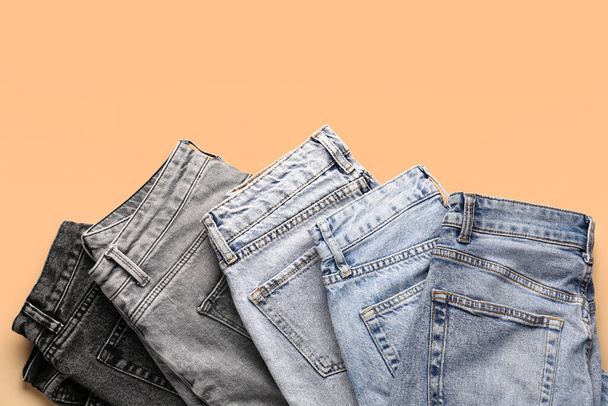 Different stylish folded jeans on pale orange background - Foto, afbeelding
