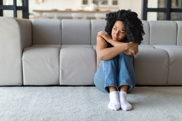 Seizoensgebonden depressie. Verontrust jonge zwarte vrouw zitten op de vloer thuis en op zoek naar opzij, verdrietig Pensive Afro-Amerikaanse vrouw lijden levensproblemen of geestelijke afbraak, gevoel eenzaam, kopiëren ruimte - Foto, afbeelding