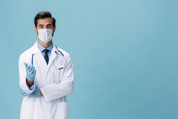 El médico con una bata blanca y una máscara médica muestra los gestos de las manos y mira a la cámara sobre un fondo azul aislado, espacio para copiar, espacio para el texto. Foto de alta calidad - Foto, Imagen