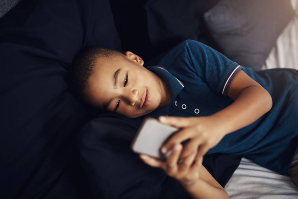 its up to you to monitor your childs smartphone use. a young boy using a cellphone while lying on his bed - Fotografie, Obrázek