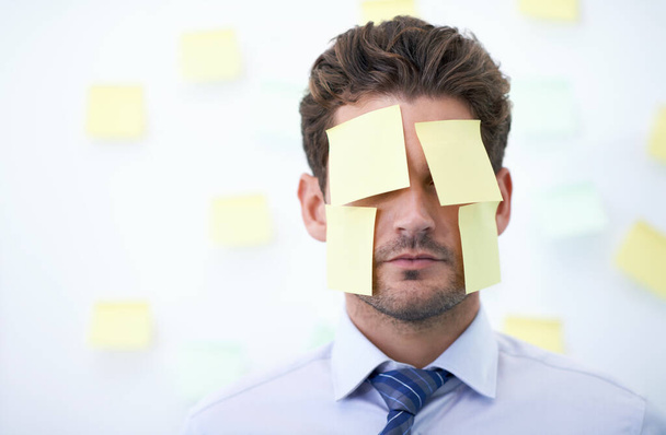 Feeling more than a little overwhelmed...a young businessman with sticky notes all over his face and in the background - Фото, изображение