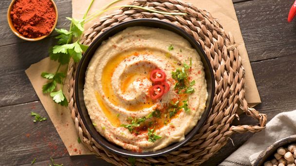 Delicious hummus in ceramic bowl. Colorful snack composition on a black wooden background. - Foto, afbeelding