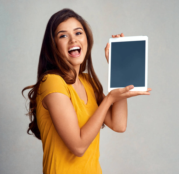 Youre going to wanna download this right now. Studio portrait of an attractive young woman holding a digital tablet with a blank screen against a grey background - Fotografie, Obrázek
