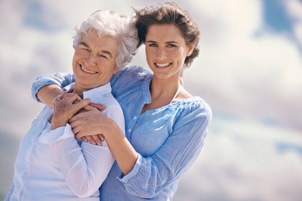 Woman, senior mother and portrait by sky with hug, happiness, love or smile for mothers day on vacation. Elderly lady, daughter or happy with care, bond or outdoor by clouds for holiday in retirement. - Foto, Imagen