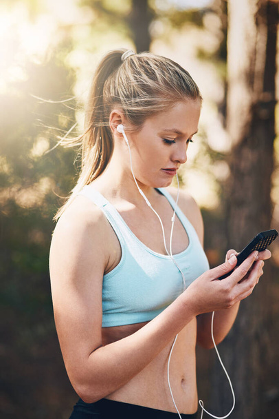 Woman with earphones, phone and fitness with music outdoor, listening for motivation on run in park. Female runner with song choice on mobile, podcast or radio streaming for exercise and health. - Photo, Image