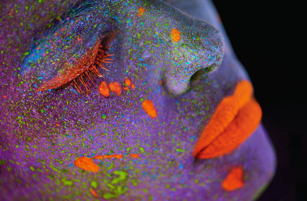 Neon paint, beauty and woman face closeup with dark background and creative cosmetics. Glow makeup, fantasy and psychedelic cosmetic of a female model with unique and creativity with art in studio. - Foto, afbeelding