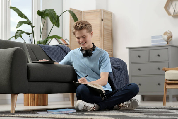 Online learning. Smiling teenage boy writing essay near laptop at home - Фото, изображение