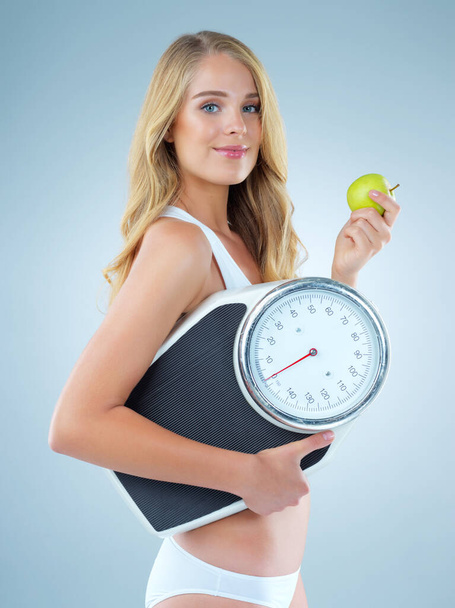 Kobieta w portrecie, jabłko w skali i schudnąć, uśmiech ze zdrowym jedzeniem izolowane na tle studio. Szczęśliwy model żeński, zdrowie i dieta z organicznych owoców z odżywiania i odchudzania. - Zdjęcie, obraz