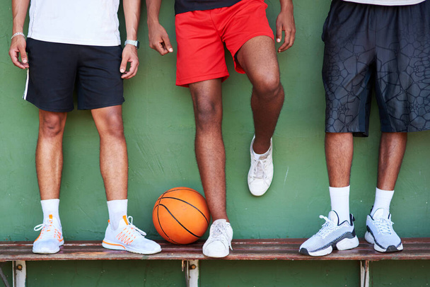 Защищай чемпионов. Крупный план группы спортивных мужчин, стоящих на скамейке рядом с баскетбольным мячом у стены - Фото, изображение