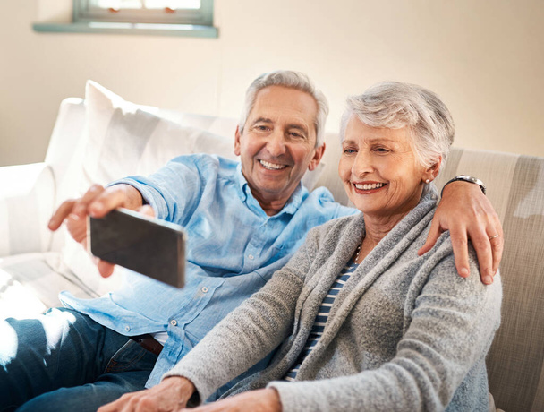 Seniorenpaar, Selfie und glücklich auf der Couch im Ruhestand für soziale Medien, Blog oder Post im Internet. Ältere Männer, Frauen und Fotografien für Profilbilder per App, Web oder gemeinsam auf dem Sofa lächeln. - Foto, Bild