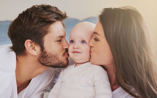Happy father, mother and kiss baby on cheek for love, care and quality time to relax together in family home. Mom, dad and kissing cute newborn kid for happiness, loving support or infant development. - Photo, Image