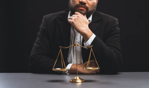 Lawyer in a black suit sits attentively on his office desk with a golden scale balance, symbol of legal justice and integrity, balanced and ethical decision making in the court of law. equility - 写真・画像