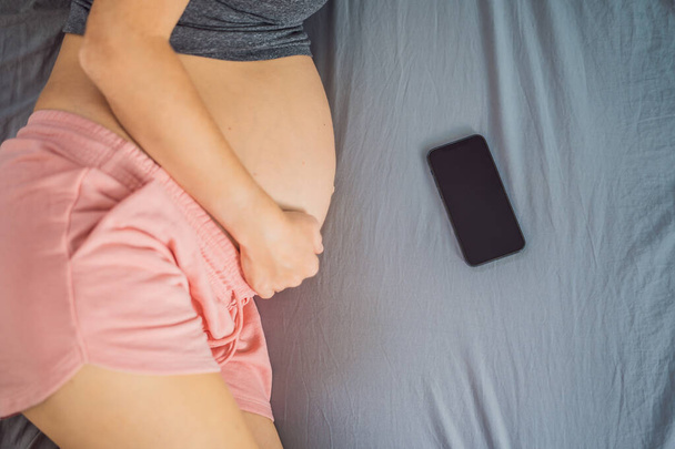 Schwangerschafts-Attrappe Mobile Schwangerschaftsanwendung im Internet. Schwangere Mutter mit Handy-Attrappe. Schwangerschaft, Medizin, Pharmazie, Gesundheitswesen und Personenkonzept. - Foto, Bild