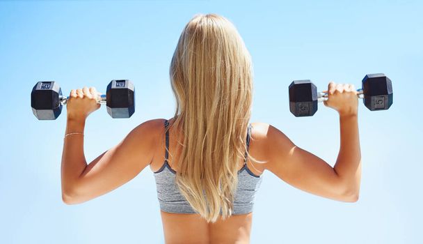 Lift and lift again. Rearview shot of young woman exercising with dumbbells outside - Foto, Imagen