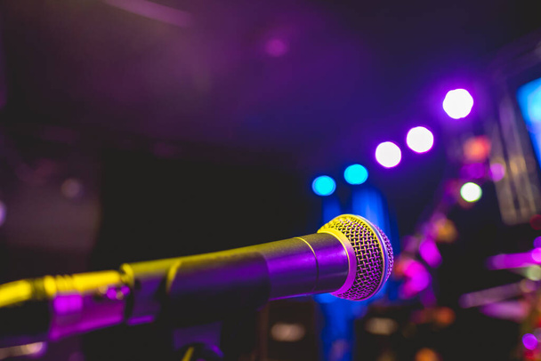 Красочное музыкальное представление: крупный план микрофона на сцене с яркими фиолетовыми и голубыми огнями в ночное время - Фото, изображение