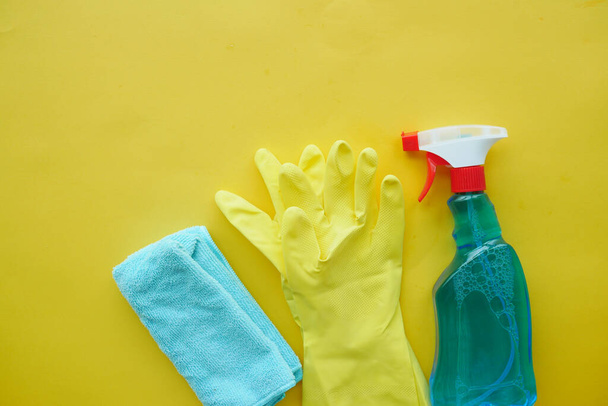 πλαστικό μπουκάλι σπρέι, γάντια και πετσέτα σε κίτρινο τραπέζι , - Φωτογραφία, εικόνα