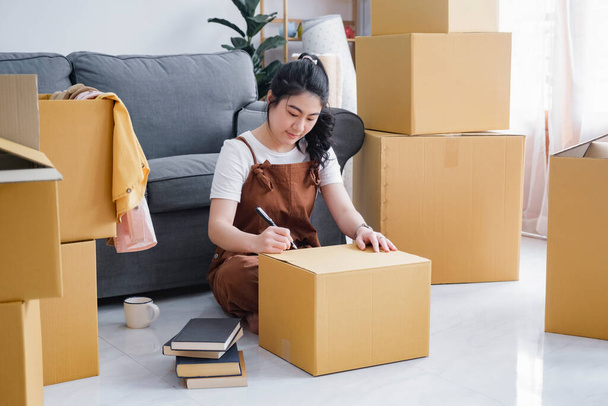 Happy single young woman packing or unpacking cardboard boxes while moving to new house or new apartment. New beginnings emotion. Living alone. Modern female people in moving home apartment leisure - Zdjęcie, obraz