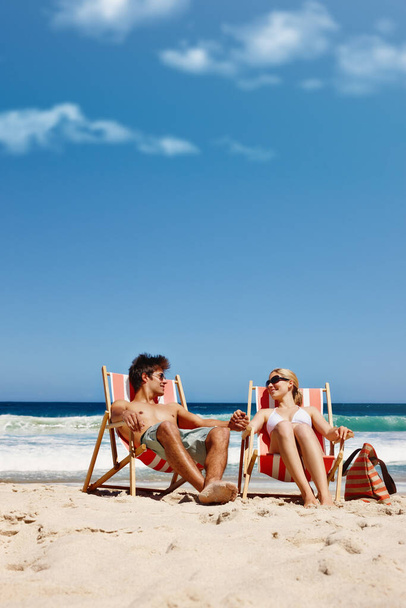¿No es ésta la vida? una feliz pareja joven reclinada en sus tumbonas en la playa - Foto, imagen