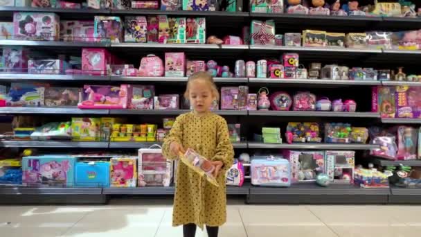 Menina escolhe um conjunto de brinquedos coloridos em um supermercado. Imagens 4k de alta qualidade - Filmagem, Vídeo