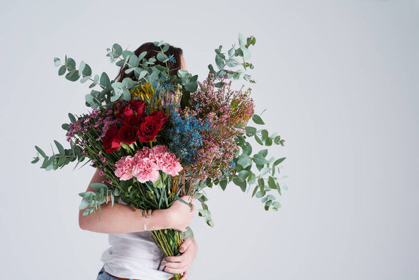 Natural, gift and woman with flowers, spring and eco friendly against grey background. Female person, model and girl with a floral present, bouquet or hide face with sustainability, nature and plants. - Fotó, kép